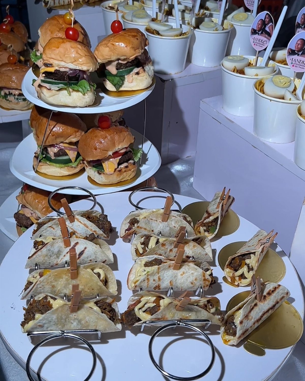 Mini sliders, tacos, and boiled eggs arranged as party appetizers on white platters.