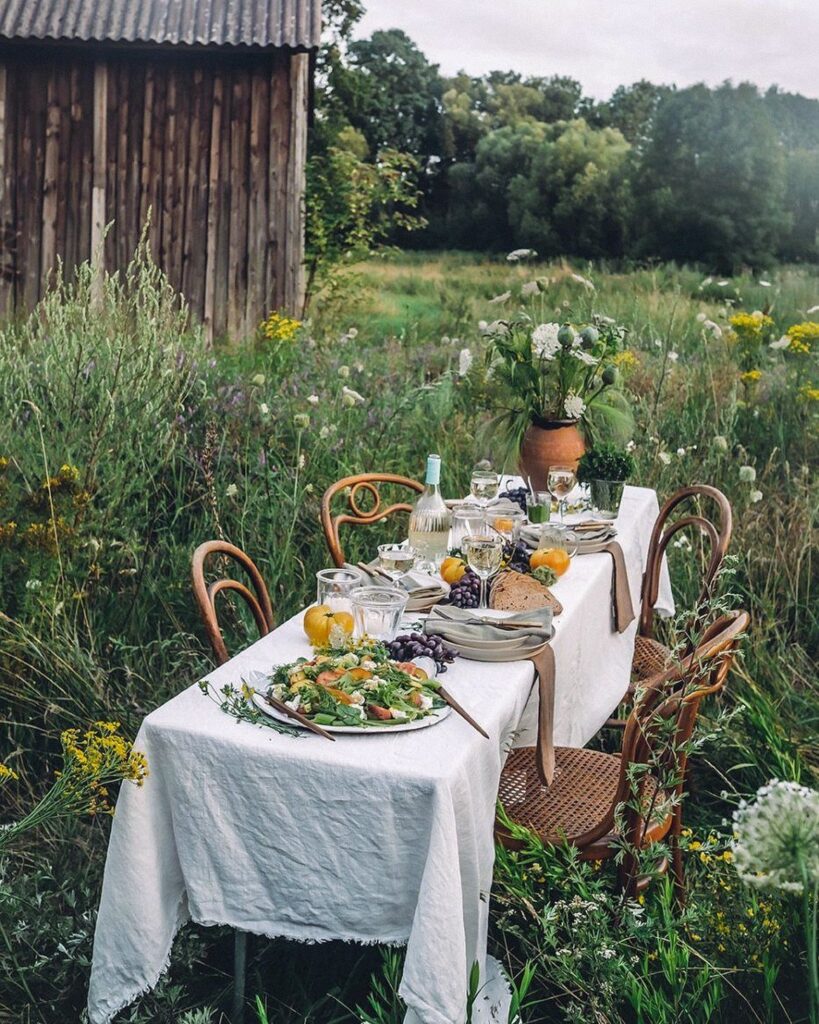 Dinner table with white linen and food set in a wild grassy field
