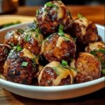 Glazed meatballs in a white bowl topped with creamy sauce and green onions.