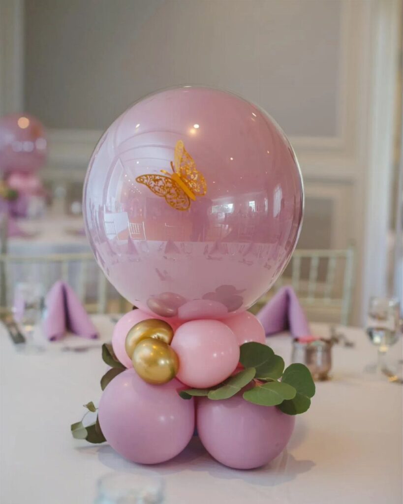 Balloon centerpiece with a gold butterfly inside a pink balloon on a table