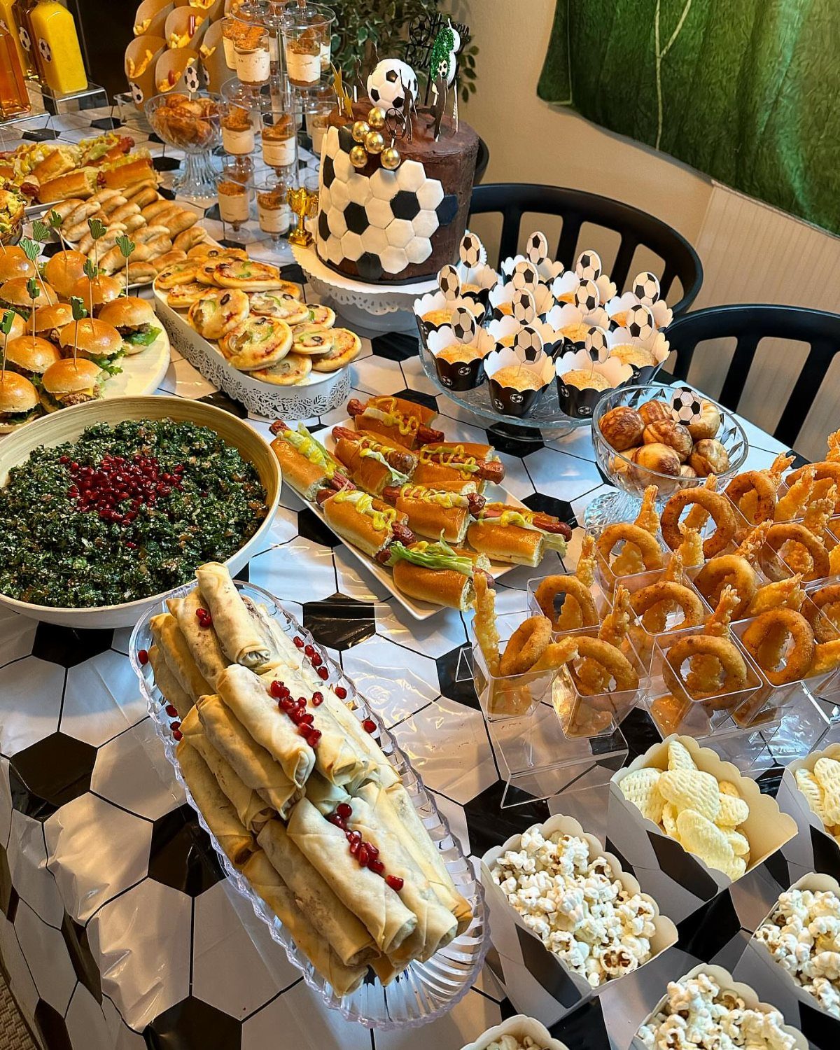 Buffet table with mini burgers, spring rolls, popcorn, and a soccer ball cake.