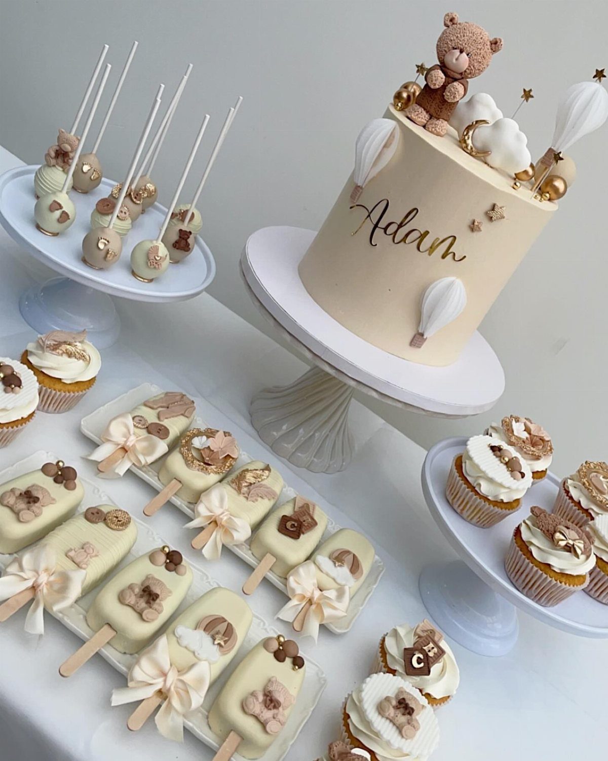 Dessert table with a teddy bear cake, cake pops, and decorated cupcakes.
