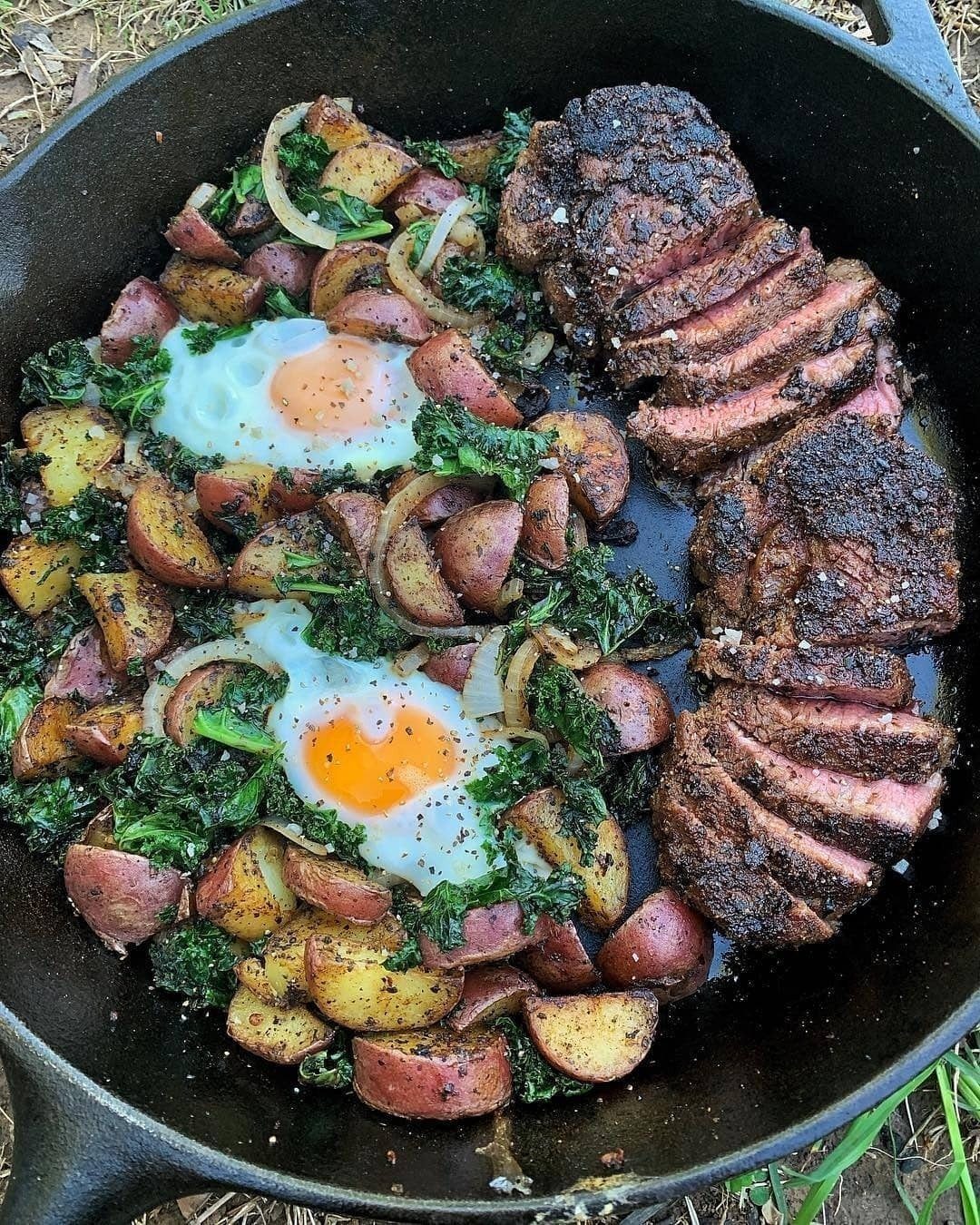 Sliced steak, fried eggs, and roasted potatoes in a cast iron skillet outdoors.