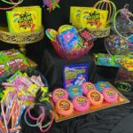 Colorful candy table display with various sweets, gold stands, and neon glow sticks.
