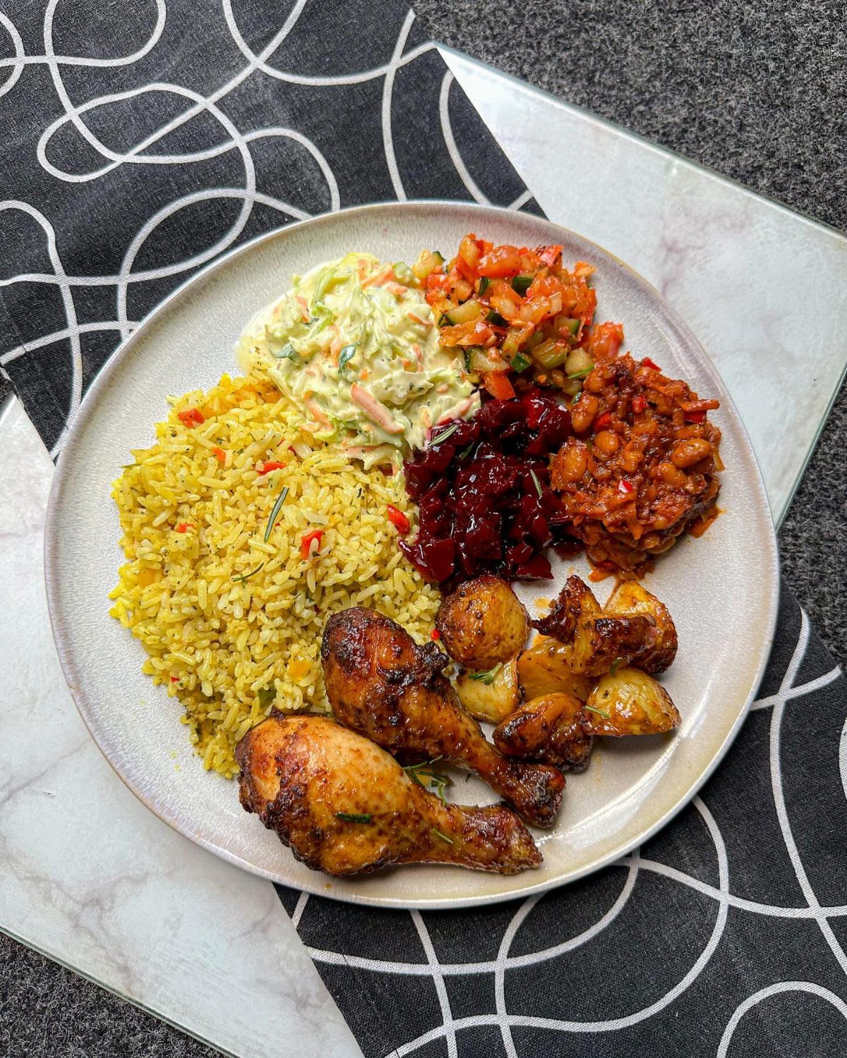 Platter of roasted chicken, yellow rice, potatoes, and various side salads on a table.