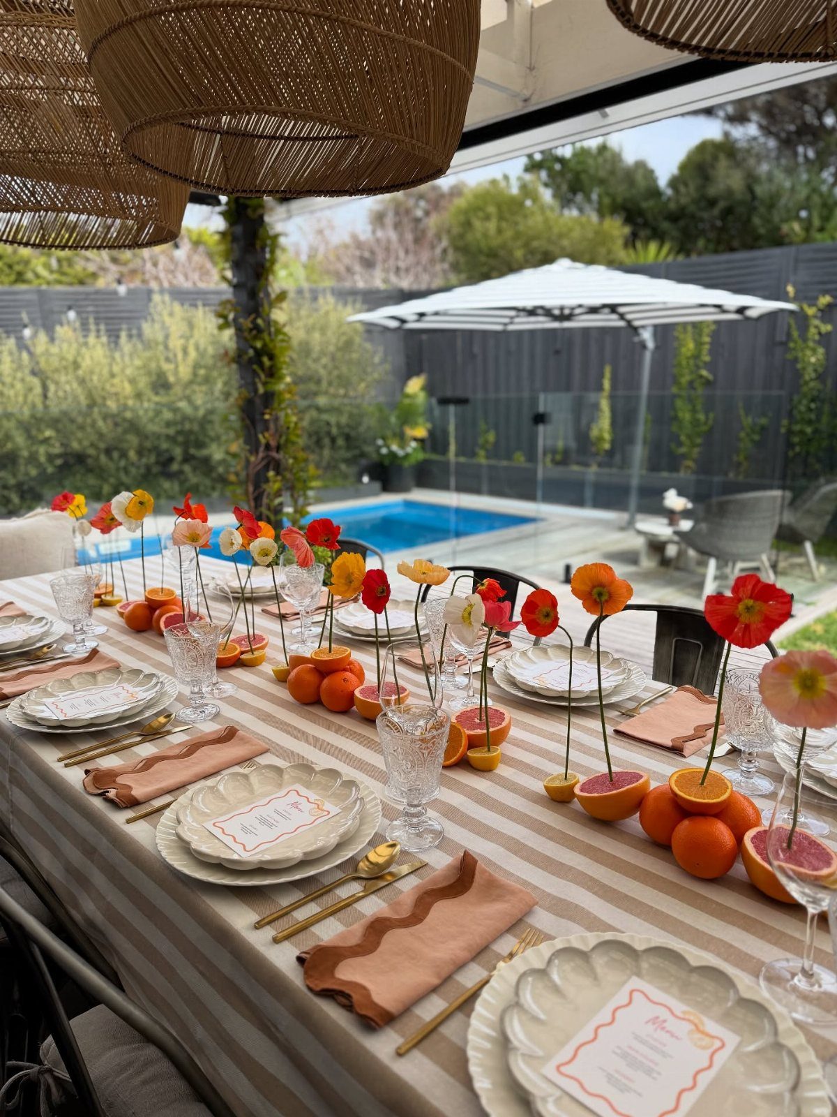 Outdoor dining table with orange and peach themed place settings and citrus centerpieces.