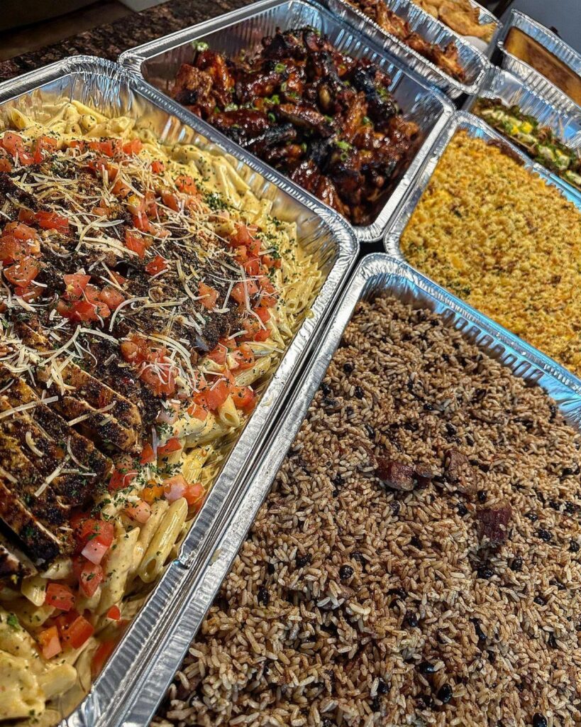 Aluminum foil trays filled with pasta, glazed meat, and rice for catering.