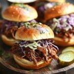 Pulled pork sandwiches with coleslaw on brioche buns served on a wooden platter.