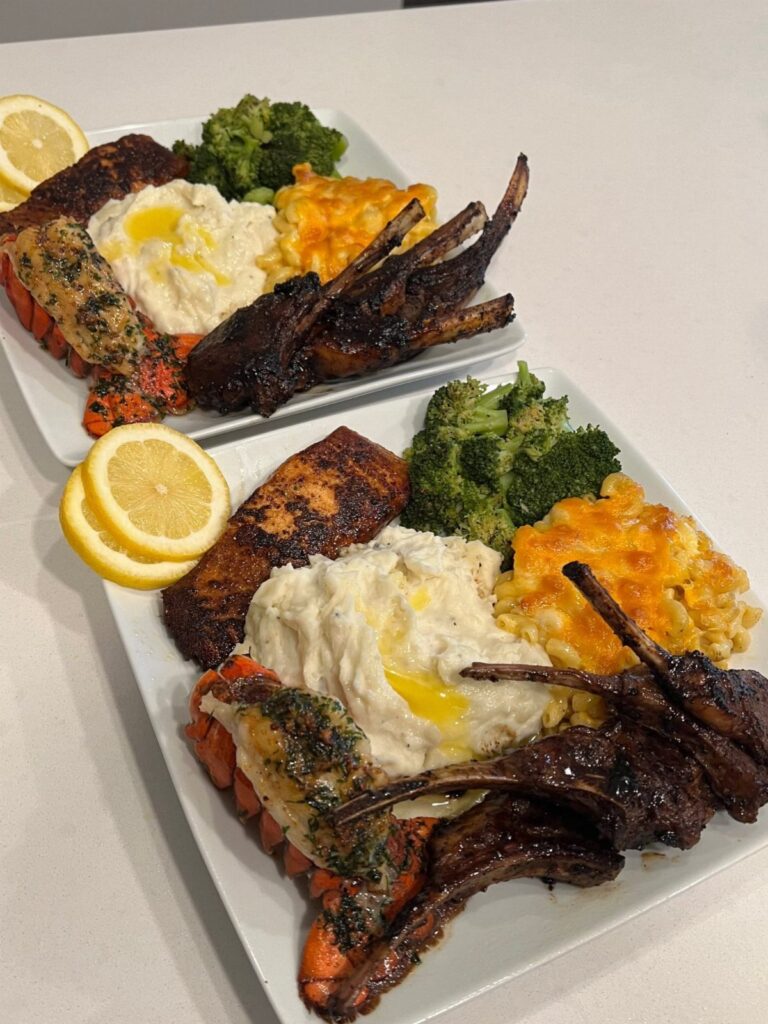 Two plates of surf and turf dinner with lamb, salmon, and vegetables.