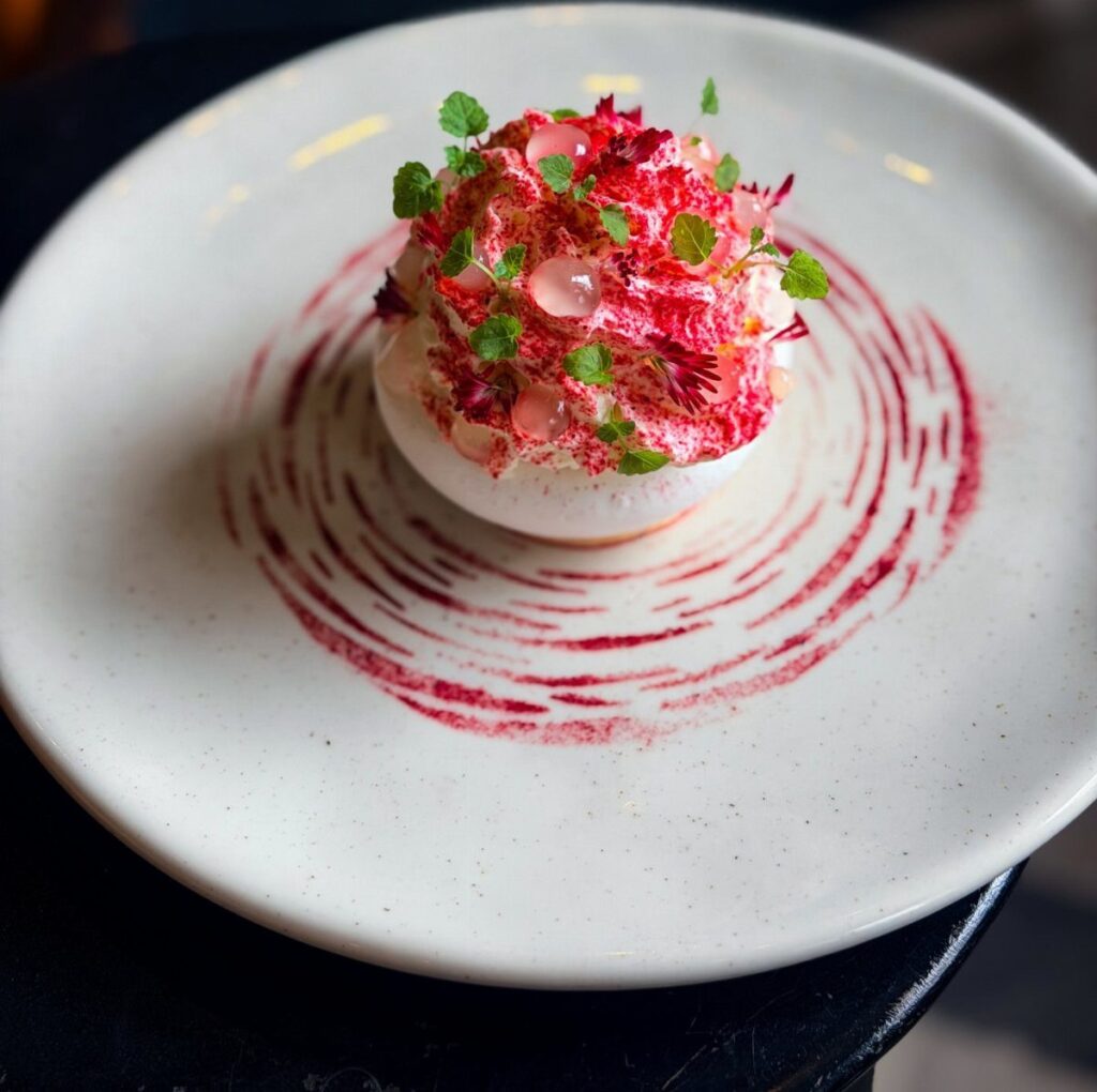 Individual pavlova dessert with pink cream and berries on a swirled white plate