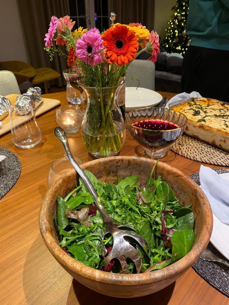 Wooden bowl of green salad and a quiche on a dinner party table.