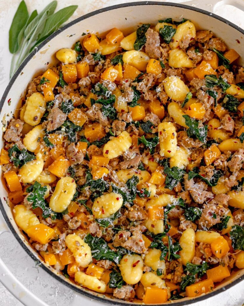 Gnocchi with squash, sausage, and kale in a white pot with sage leaves.