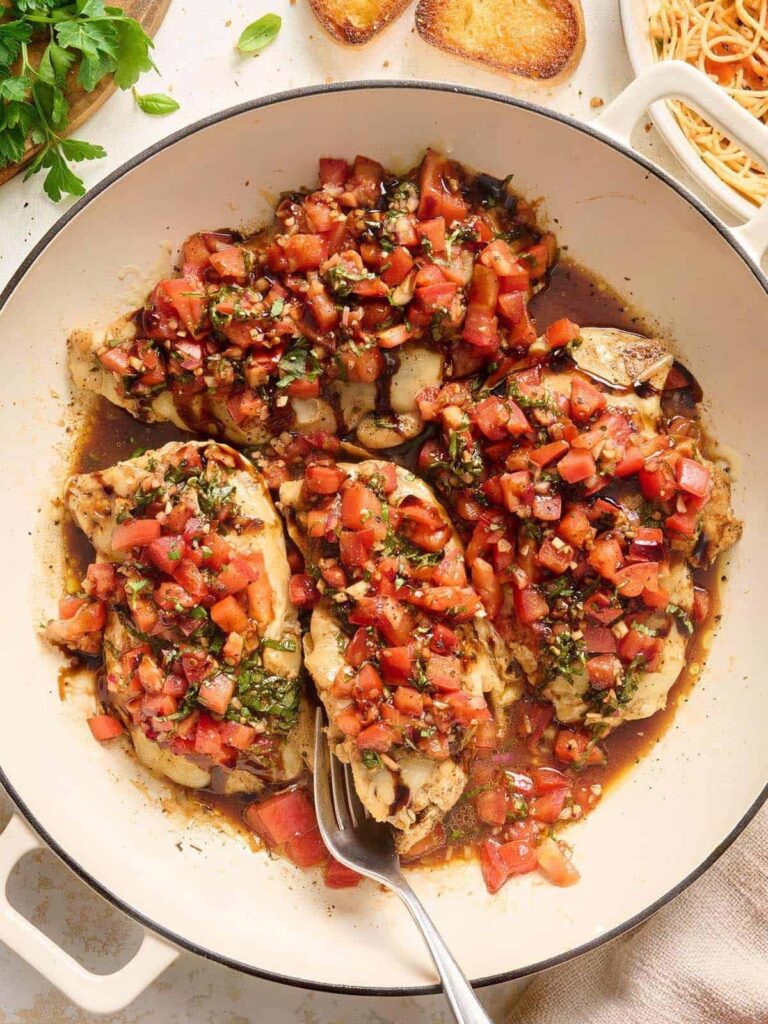 Chicken breasts topped with fresh tomato bruschetta in a white skillet pan.