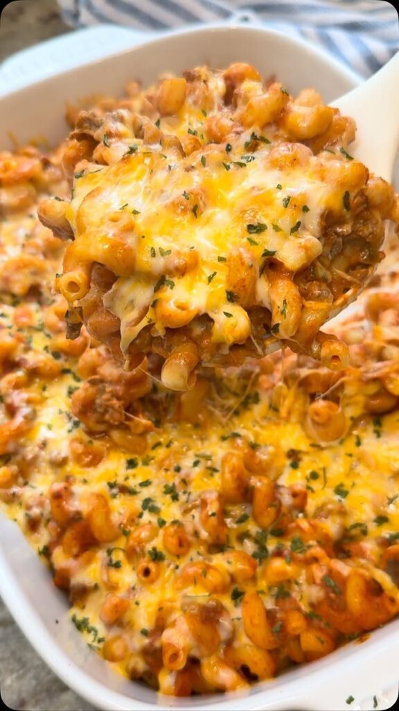 Cheesy macaroni and meat casserole in a white dish with a serving spoon.
