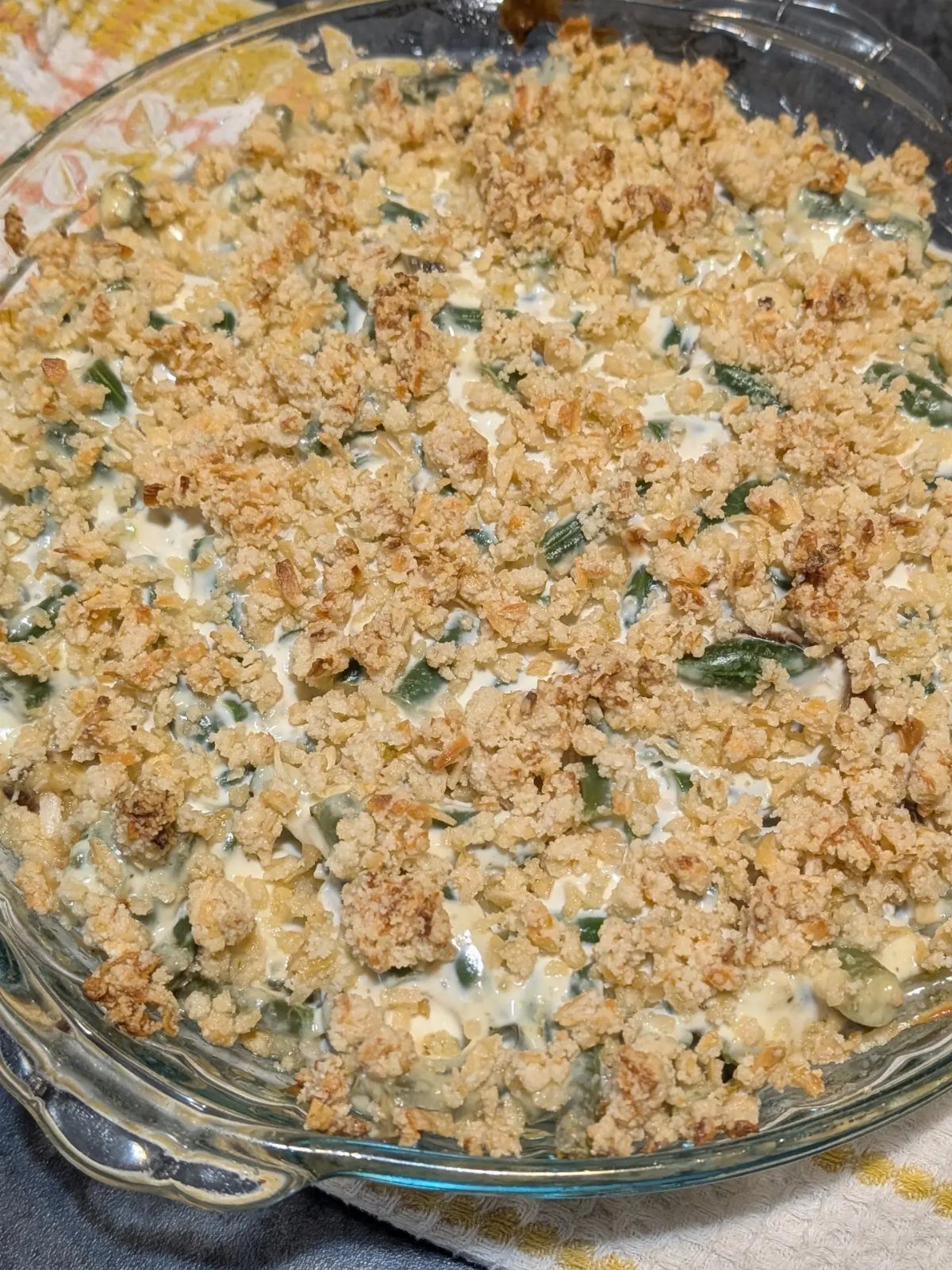 Green bean casserole with crispy onion topping in a clear glass baking dish.