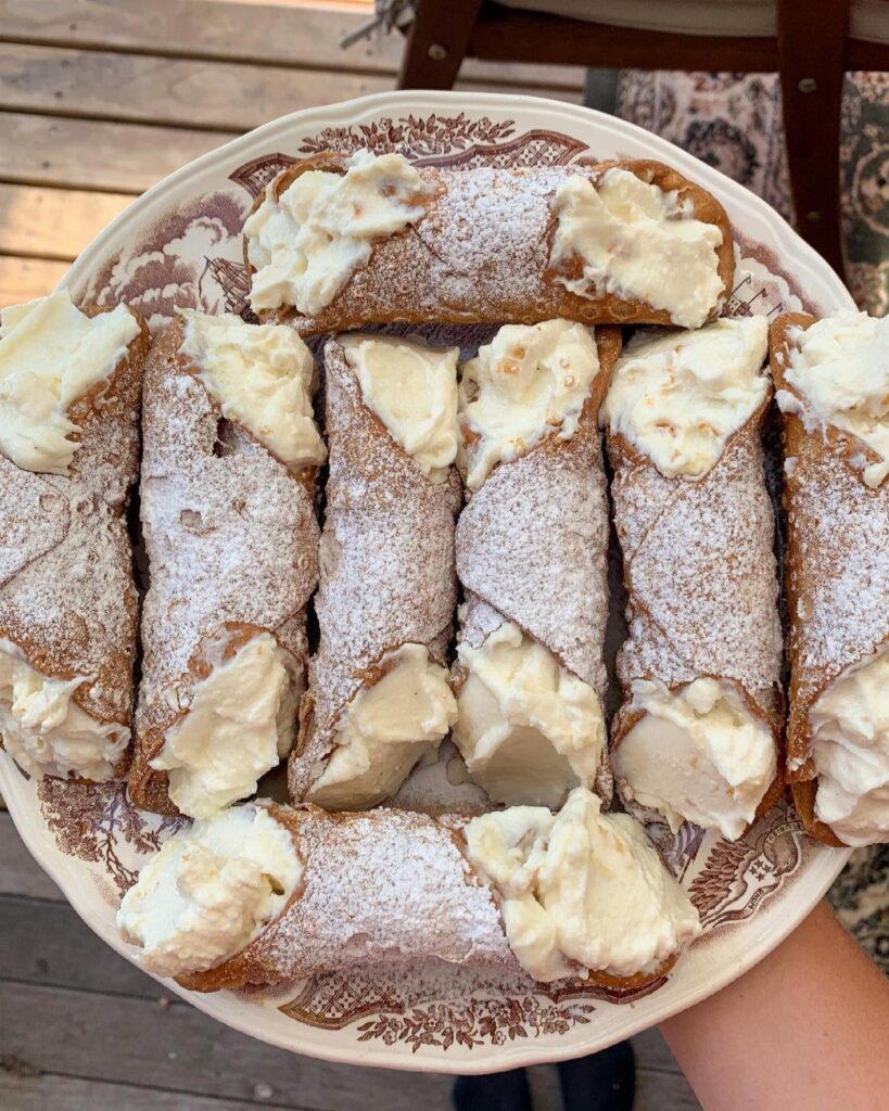 Cannoli with ricotta cream and powdered sugar on a decorative white plate.