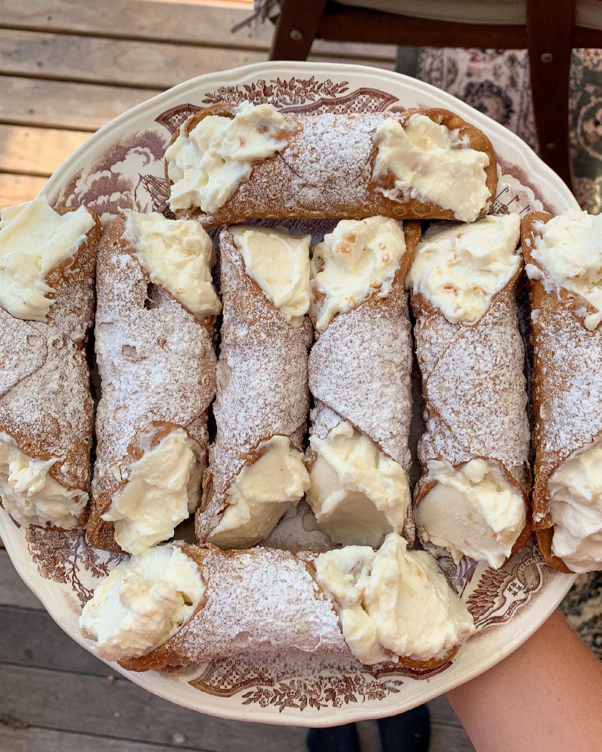 Cannoli with ricotta cream and powdered sugar on a decorative white plate.