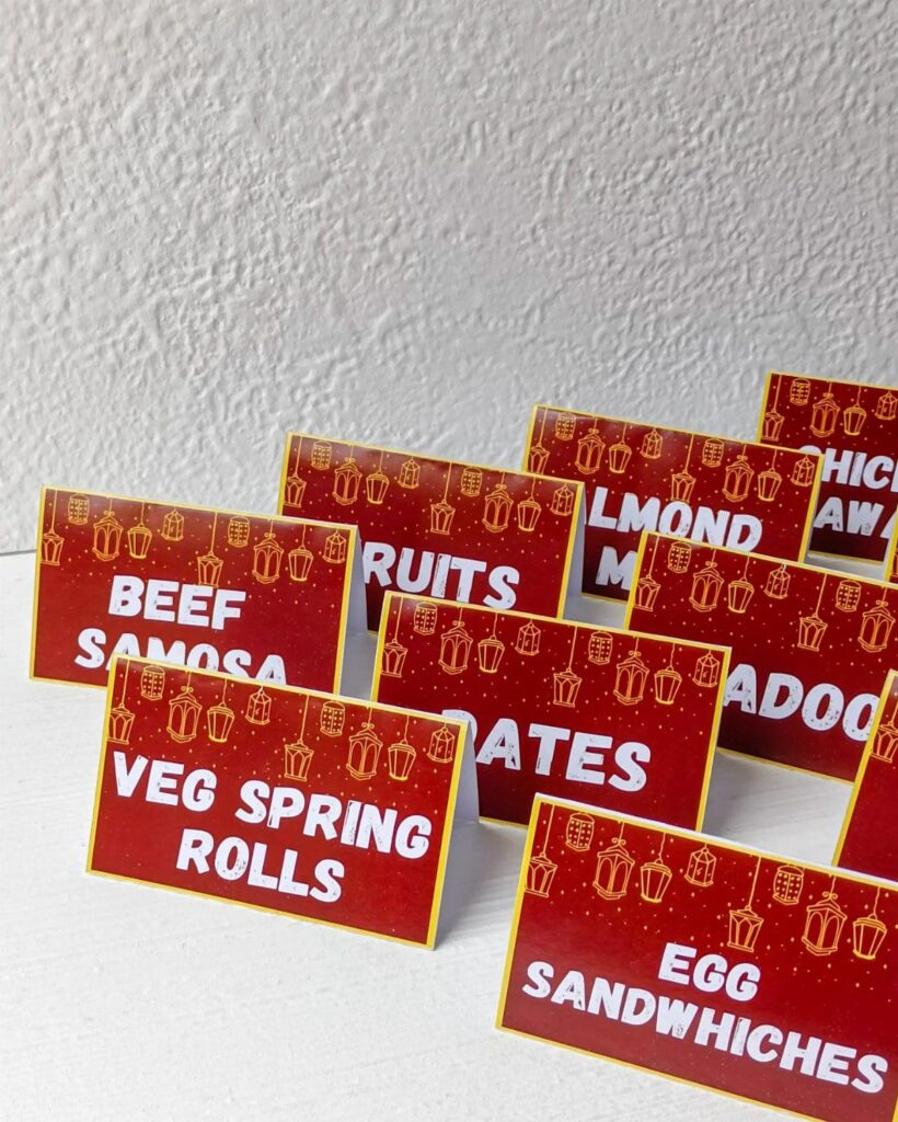 Red party food labels with white text and gold lanterns on white surface