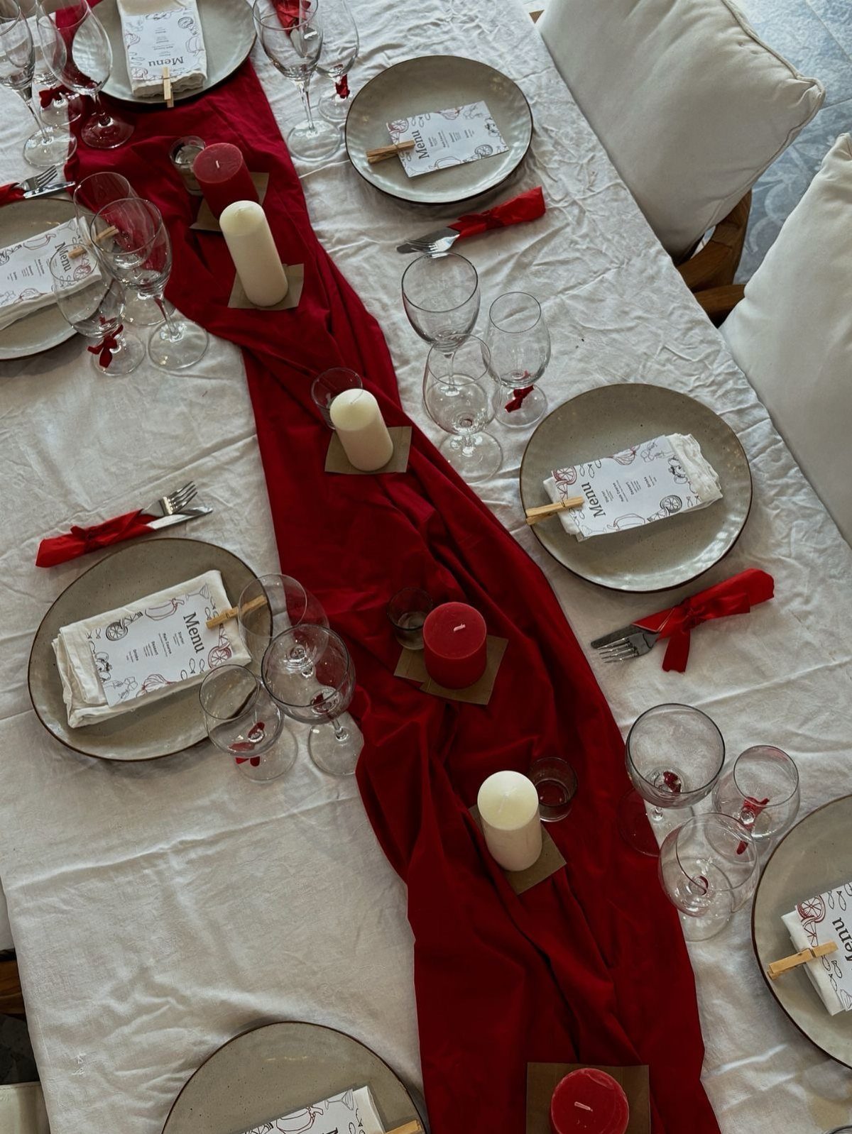 Dining table with white cloth, red runner, grey plates, and pillar candles.