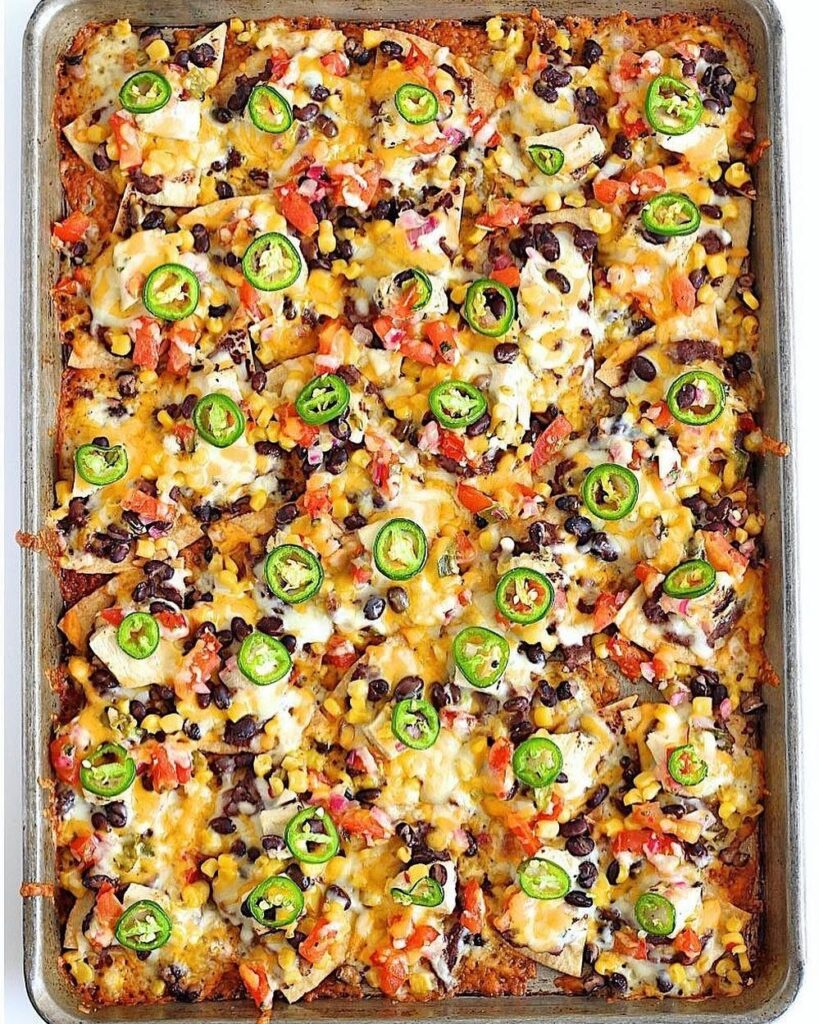 Sheet pan nachos topped with melted cheese, black beans, corn, and jalapeño slices.