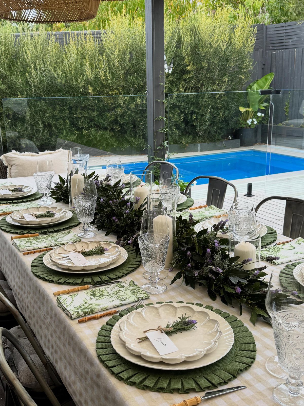 Elegant outdoor table place settings with white plates, green placemats, and greenery runner.