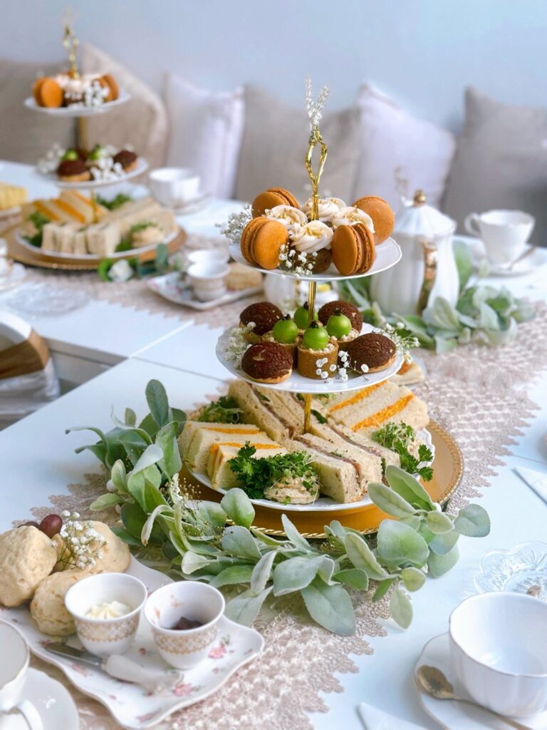 Three-tiered stand with macarons and sandwiches on a decorated white tea party table.