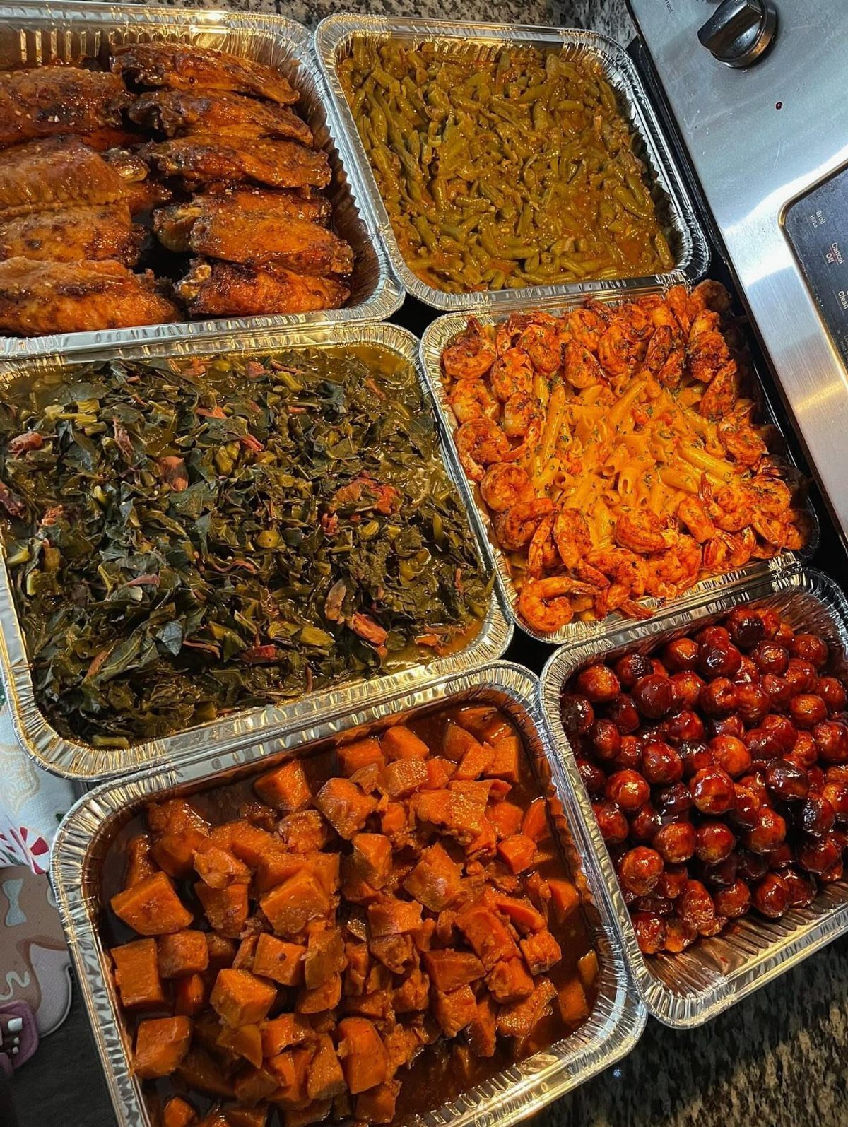 Assorted Thanksgiving side dishes and chicken wings in aluminum foil catering trays.