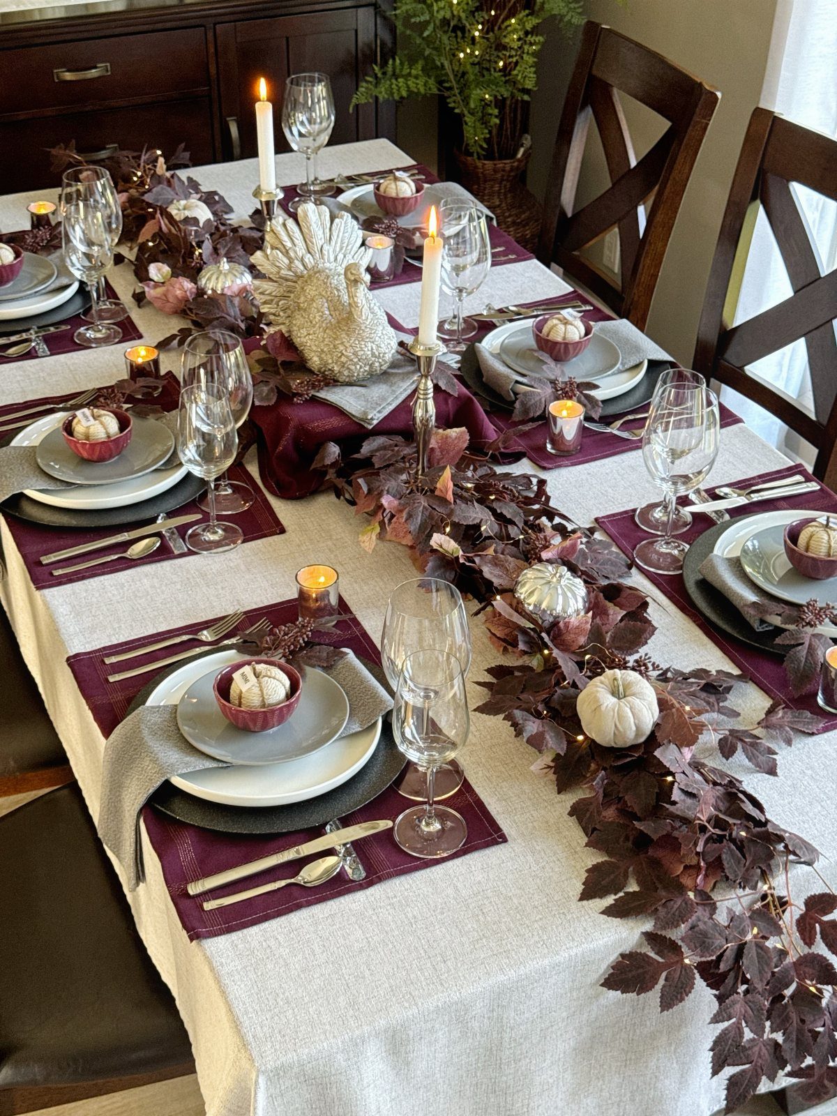 Layered plates and grey napkins on a Thanksgiving table with autumn leaf centerpiece.
