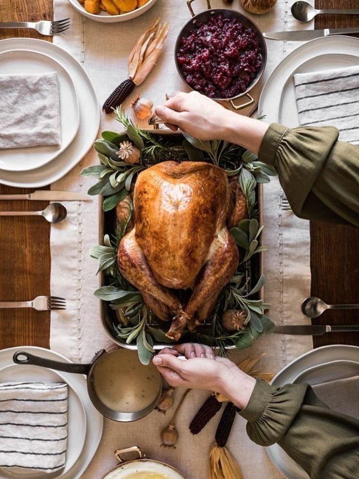Roasted turkey surrounded by sage leaves on a fully set Thanksgiving dinner table.